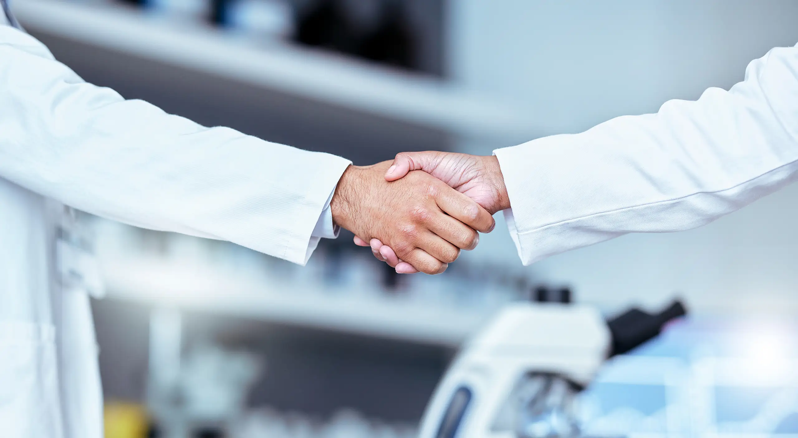 Clinical professionals shaking hands in a laboratory — medical monitoring and clinical operations